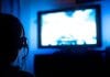 PC Gaming On A TV – A Lazy Gamer’s Guide Young male gamer with glasses and headset playing video game at home in the dark room using game console controller watching at LED TV. Gaming and entertainment concepts