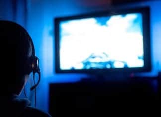 PC Gaming On A TV – A Lazy Gamer’s Guide Young male gamer with glasses and headset playing video game at home in the dark room using game console controller watching at LED TV. Gaming and entertainment concepts