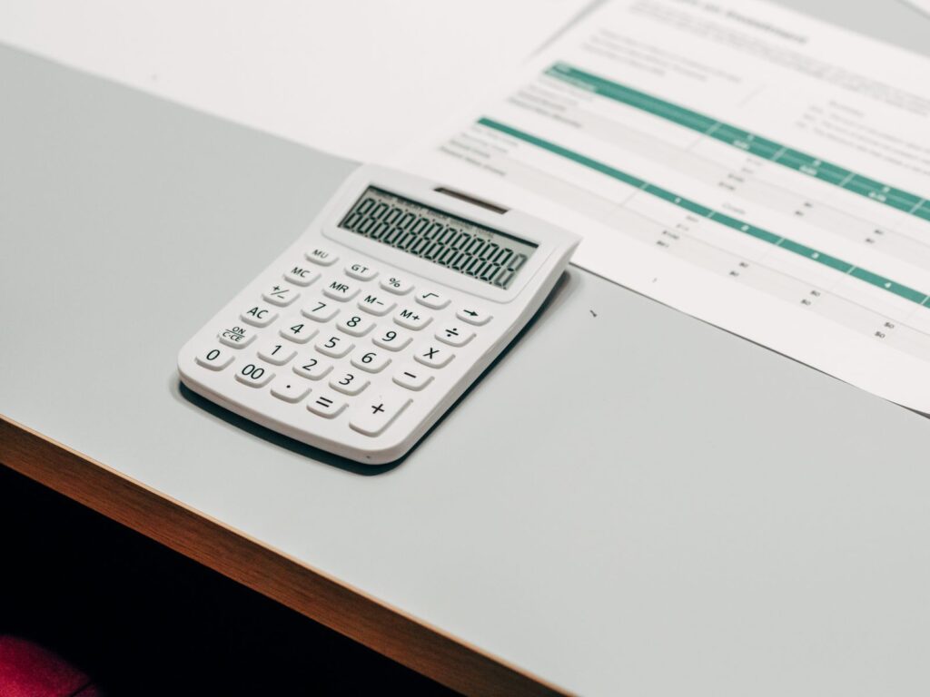 A white calculator beside a printed spreadsheet on a desk