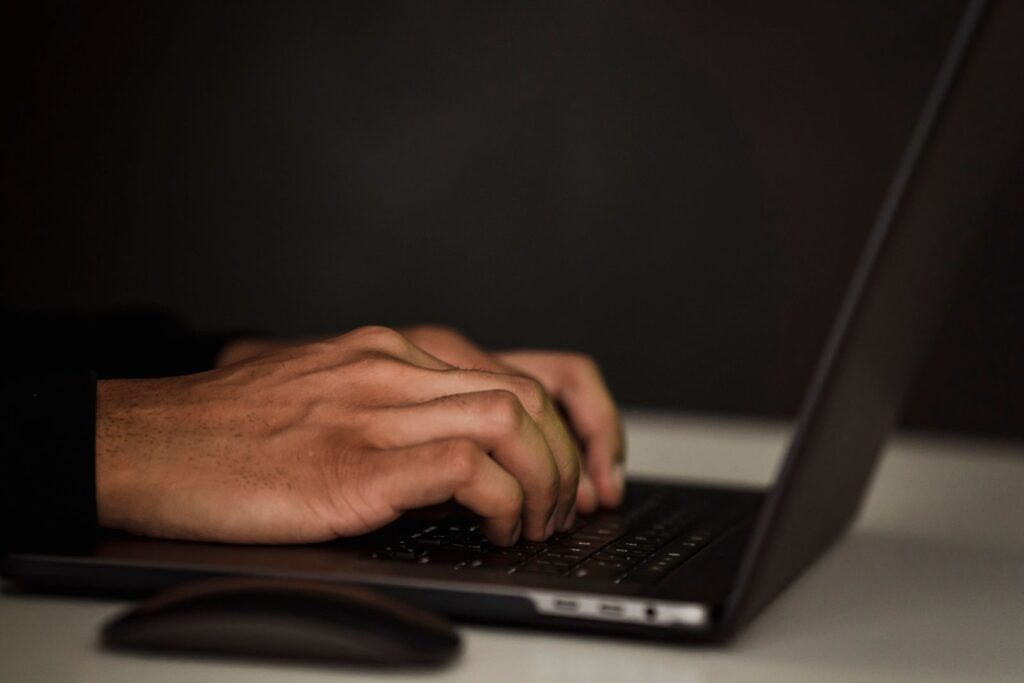 Close-up of hands typing on a laptop keyboard in a dim room