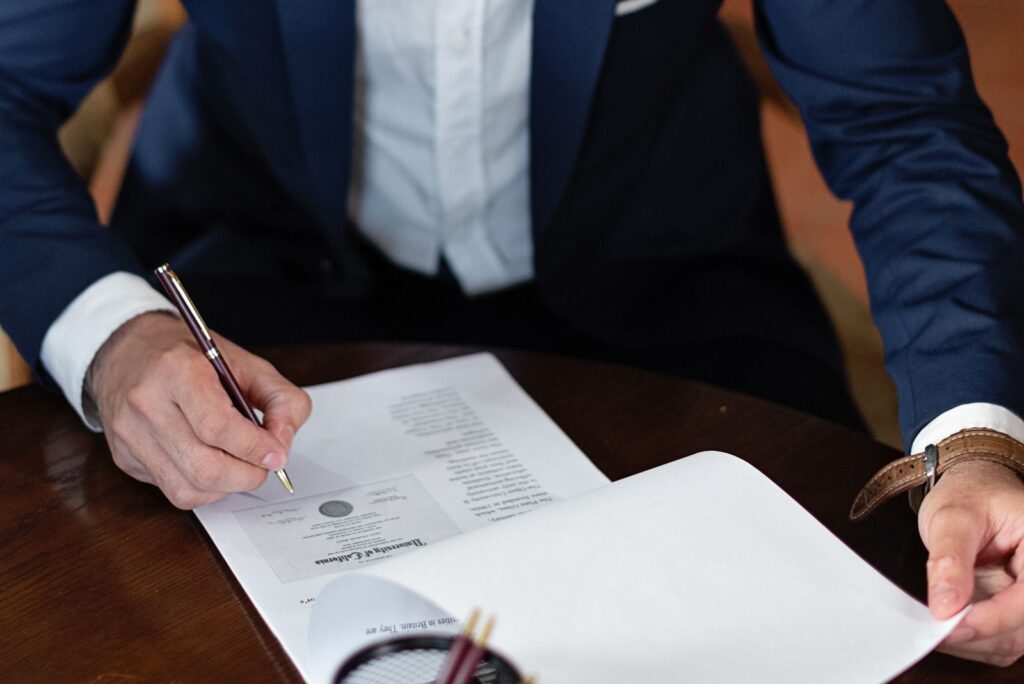 A man in a suit signing a printed document at a wooden desk