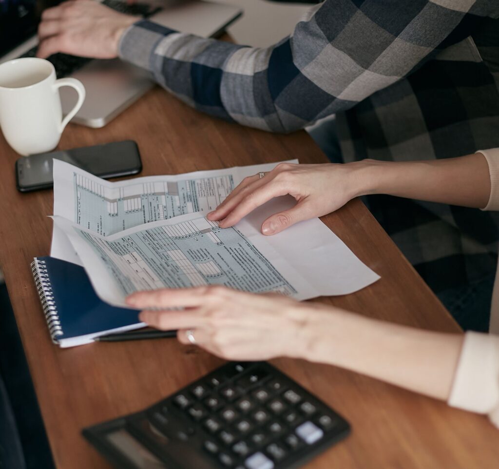 Two people reviewing printed tax forms at a desk with a phone and coffee mug