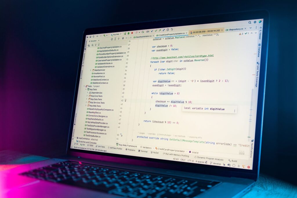 A laptop showing a code editor, lit by pink and blue light in a dark room