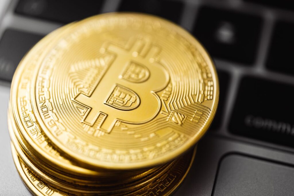 A stack of gold-coloured Bitcoin coins resting on a laptop keyboard