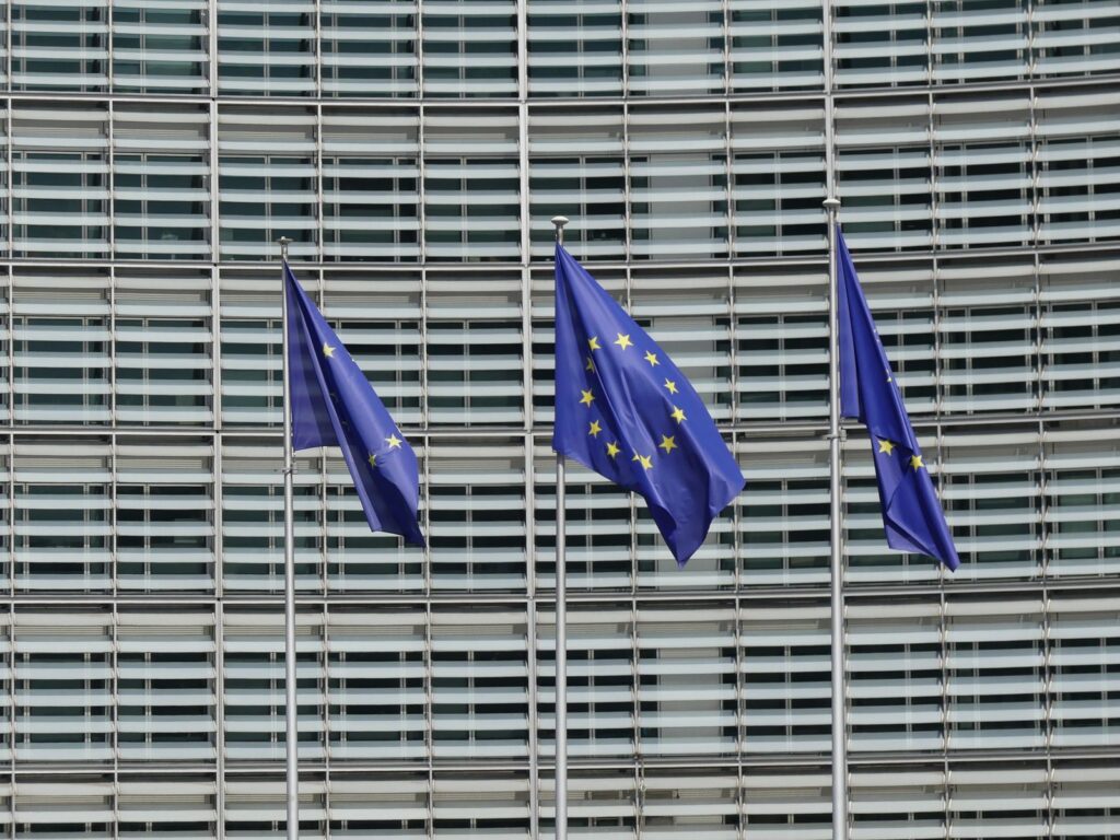 Three European Union flags on poles in front of a large glass office building