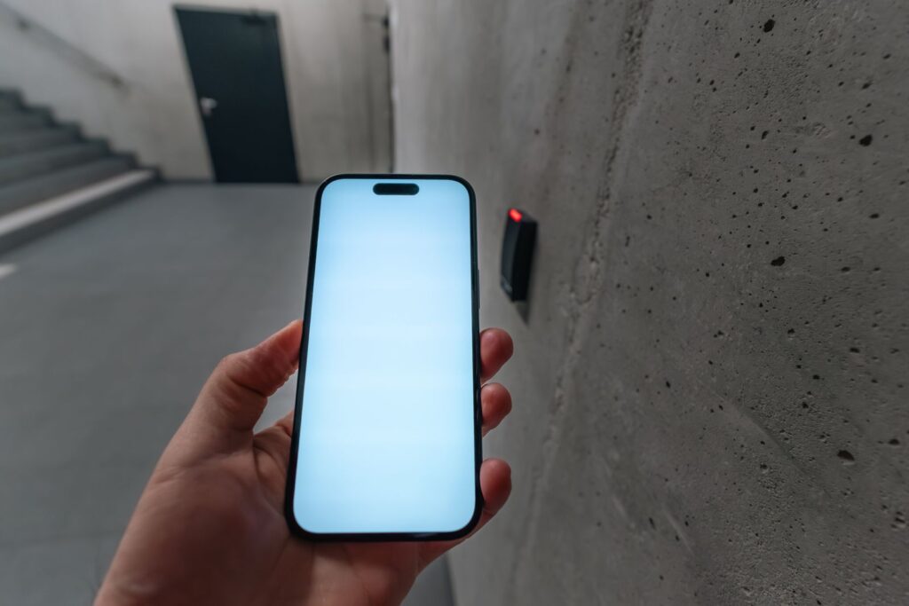 A hand holding a smartphone with a blank bright screen in a concrete stairwell