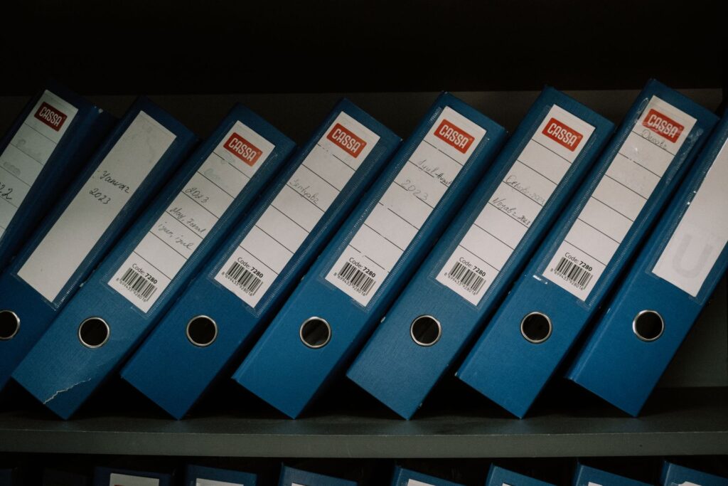 A row of blue ring binders with barcode labels on an office shelf