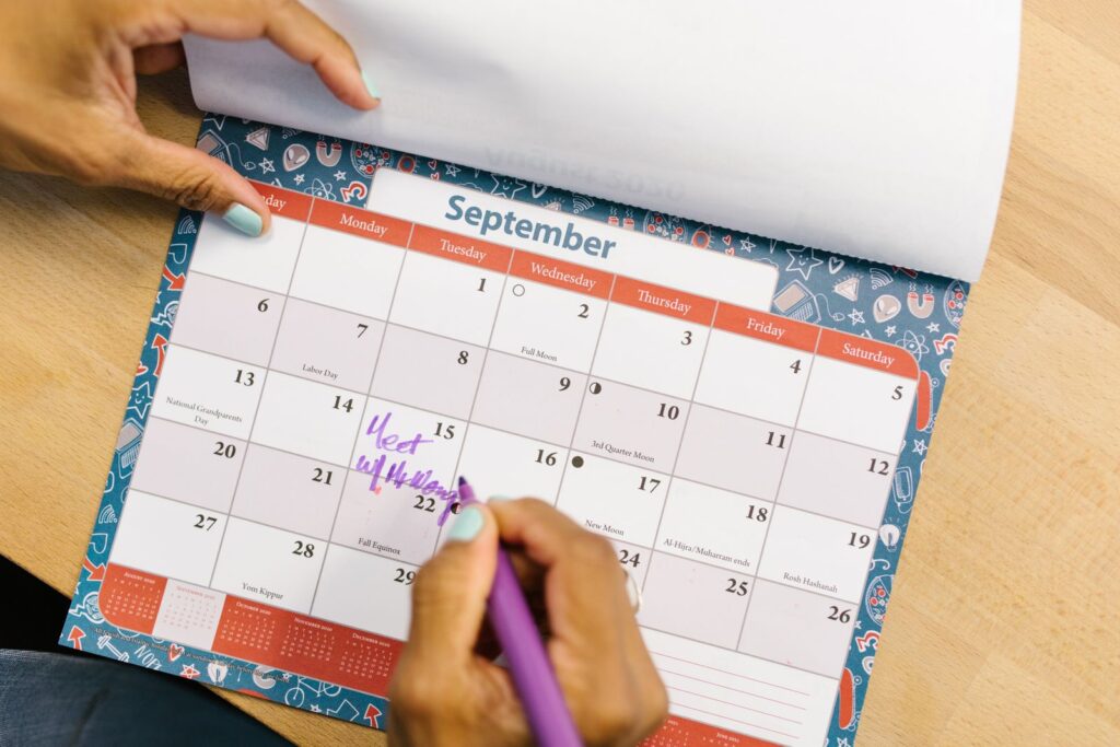 A person marking a date on a paper wall calendar with a purple pen