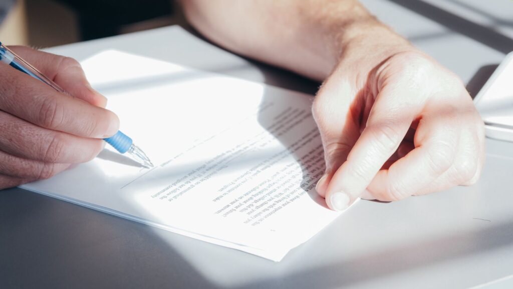 A person signing a printed document with a blue pen