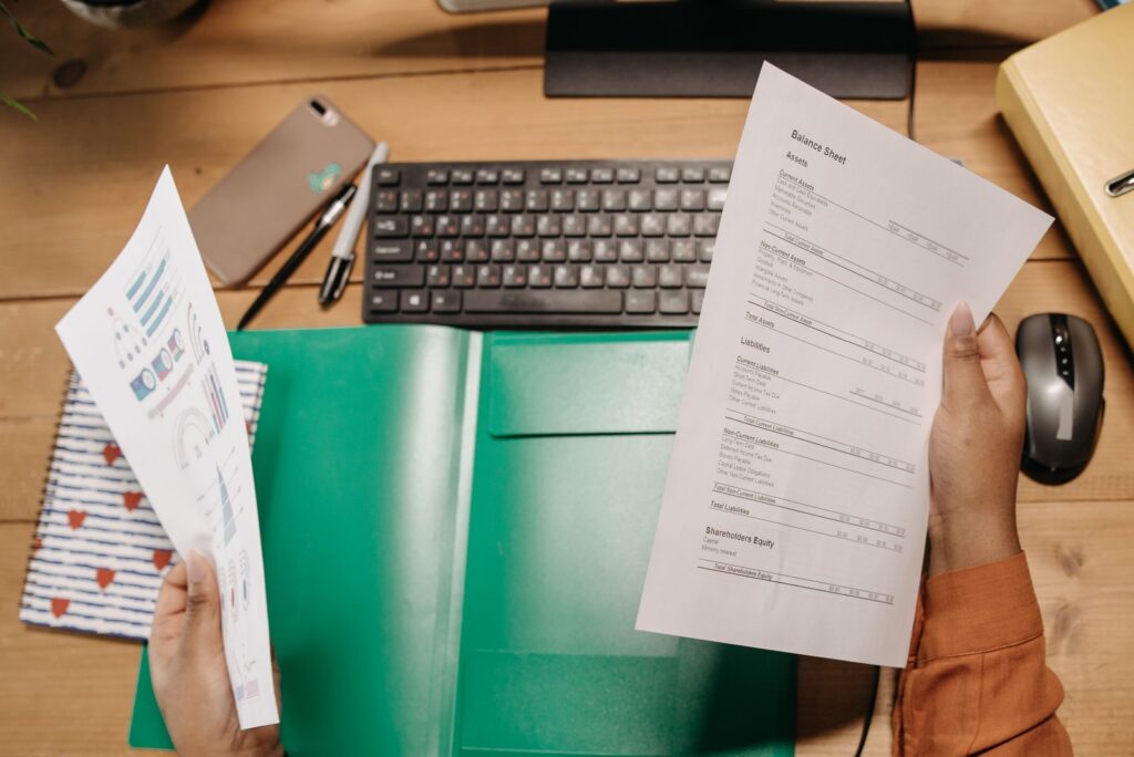 Two hands holding printed documents over a desk with a keyboard and a green folder