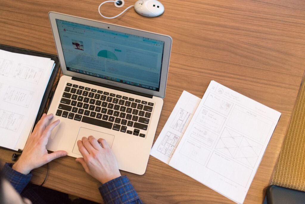 Overhead view of a person typing on a laptop beside printed notes and sketches