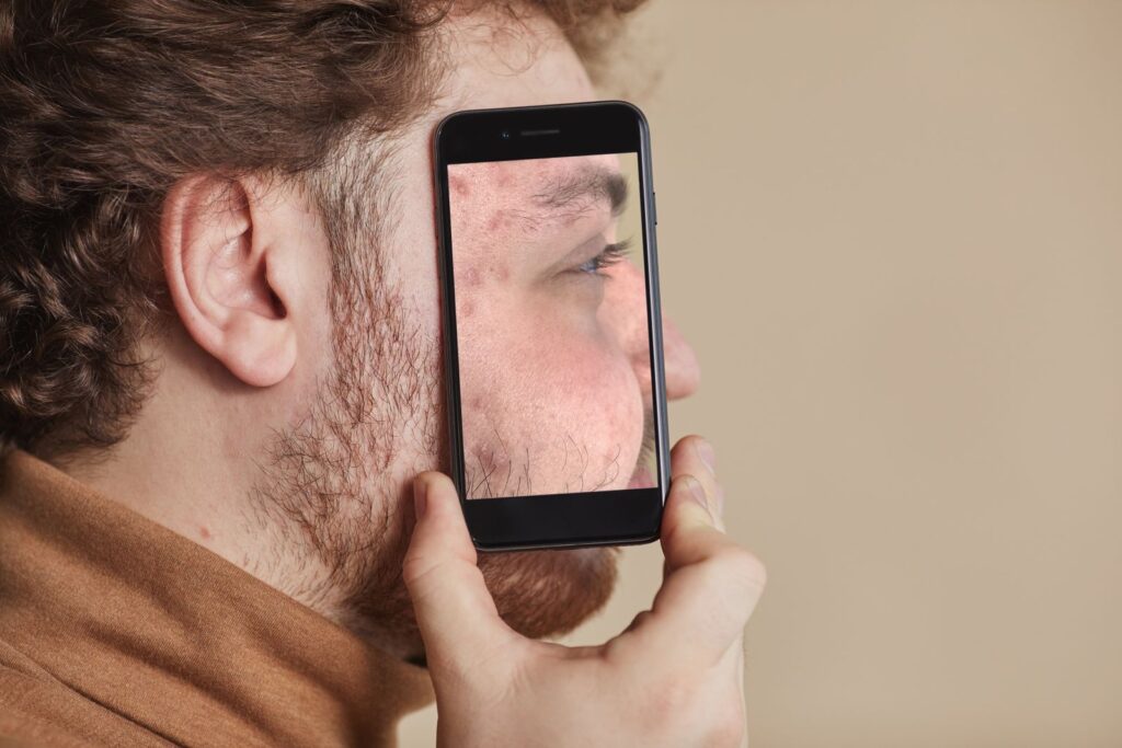 A man holding a smartphone up beside his face, the screen showing part of his face