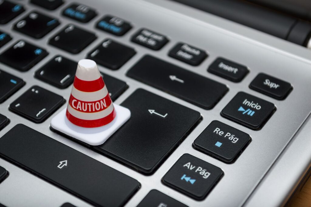 A small red and white caution cone standing on a silver laptop keyboard
