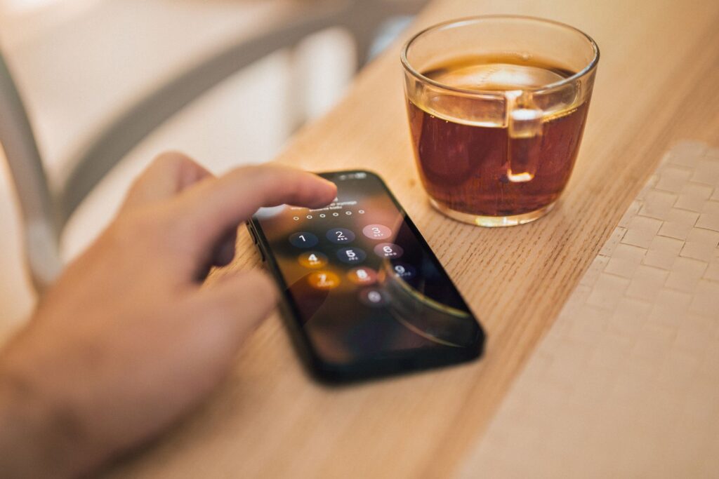 A hand unlocking a smartphone on a wooden table next to a glass of tea