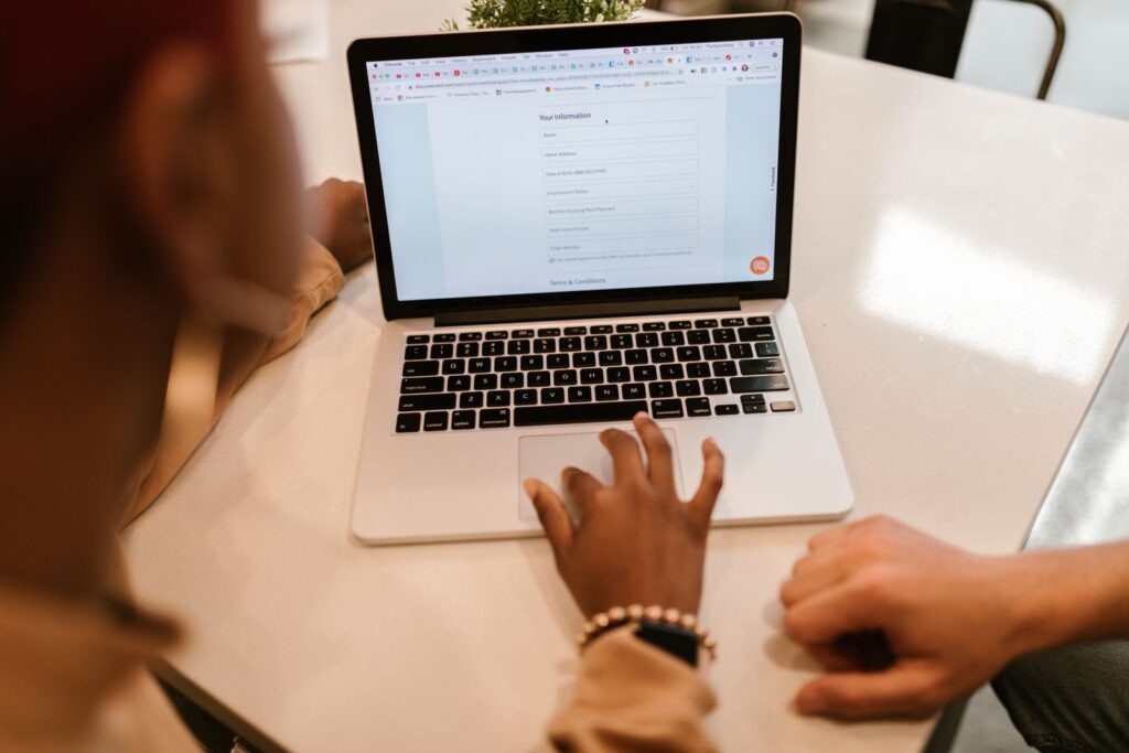 Two people at a white table, one typing into an online form on a laptop