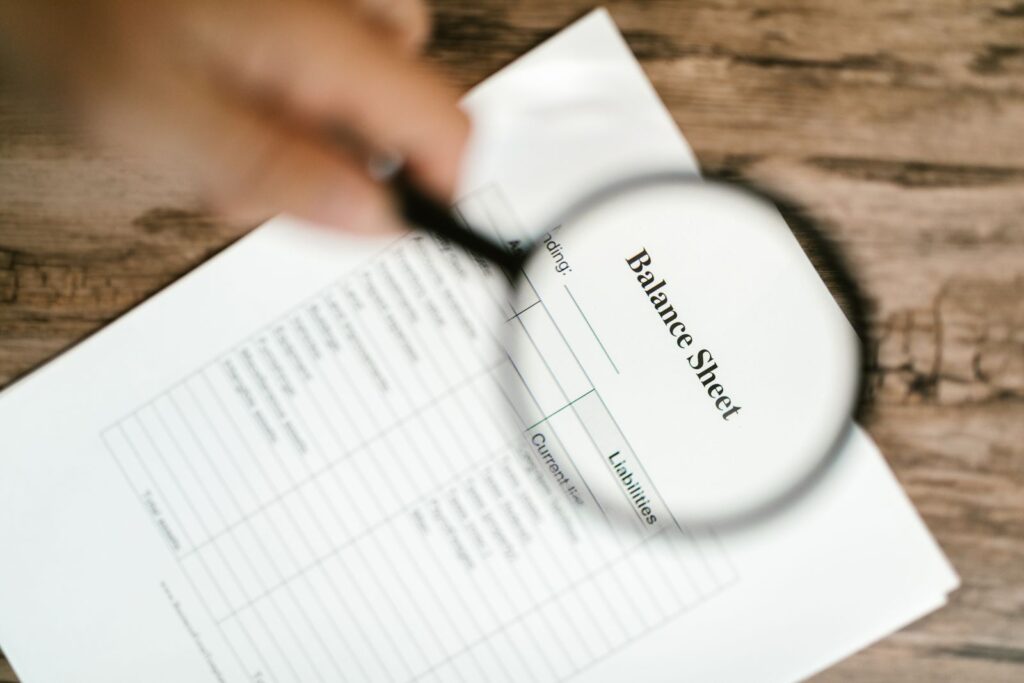 A magnifying glass held over a printed balance sheet on a wooden table