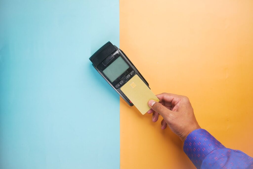 A hand tapping a plain yellow card on a black card terminal against a blue and orange background