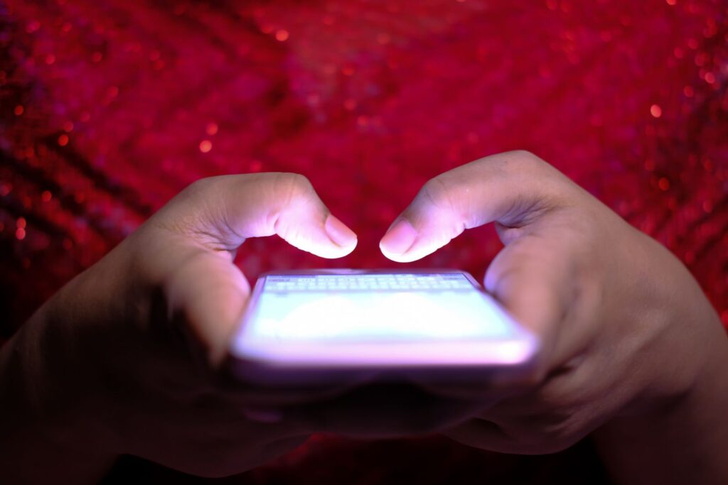 Two hands holding a glowing smartphone in low light