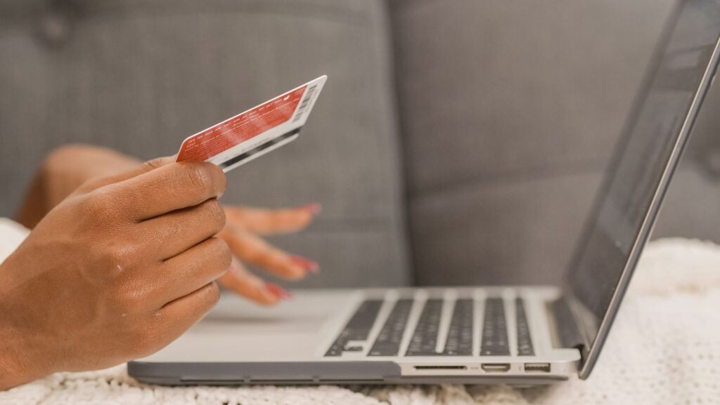 A person holding a bank card in one hand next to an open laptop