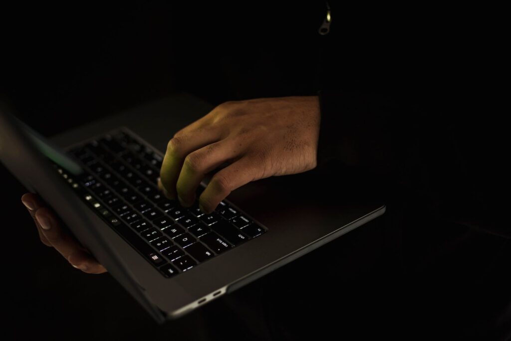 A person in a dark room typing on a laptop keyboard, face out of frame