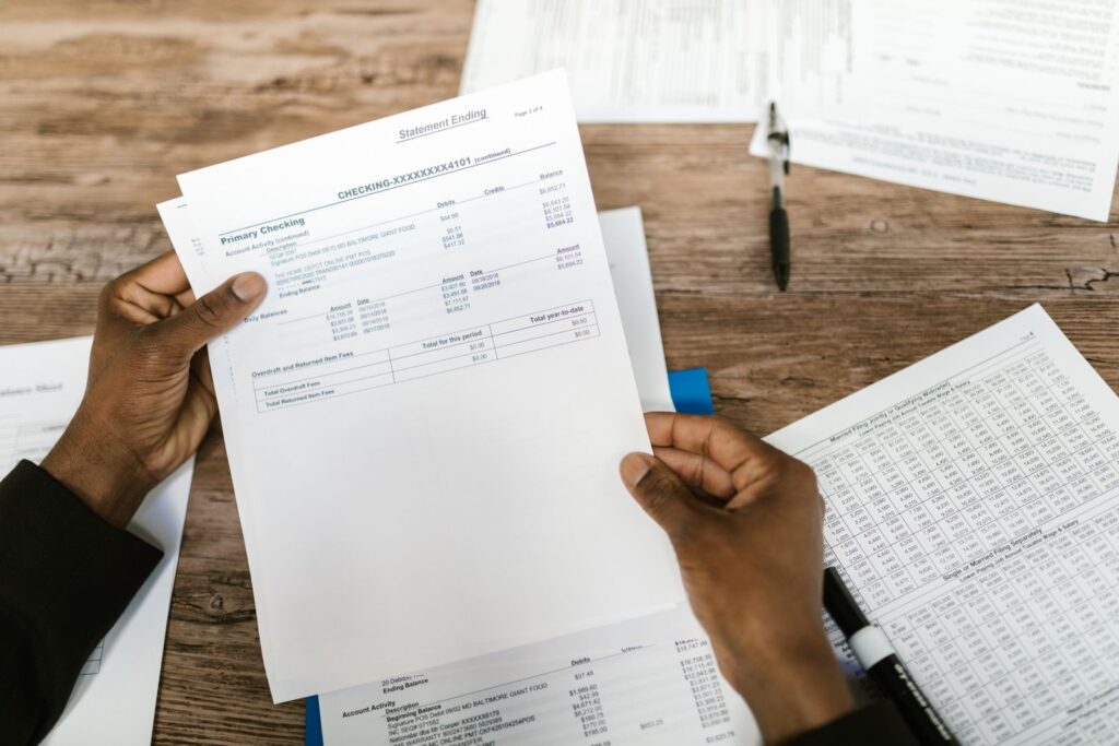 Hands holding a printed bank statement above a desk covered with financial paperwork
