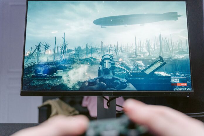 Player holding a controller in front of a monitor showing a first person shooter on a battlefield